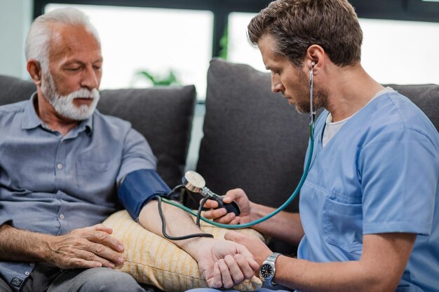 Trabajador de la salud que mide la presión arterial de un paciente maduro durante una visita a su hogar