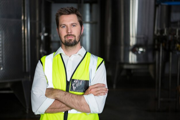 Trabajador de sexo masculino con los brazos cruzados de pie en la fábrica.