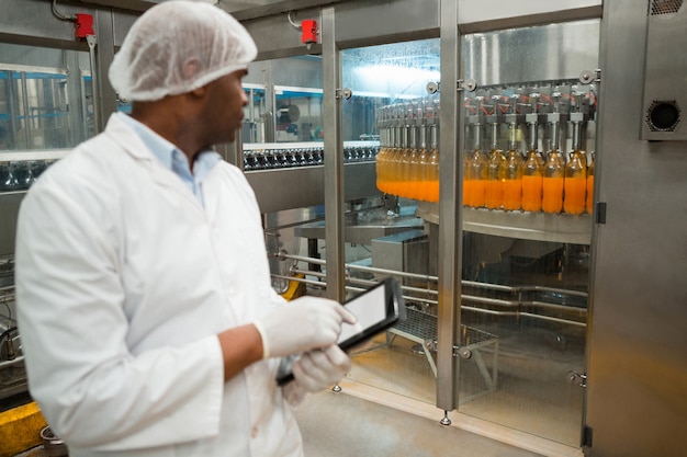 Trabajador de sexo masculino inspeccionando botellas de jugo en la fábrica.