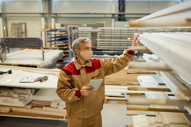 Trabajador de sexo masculino que usa el panel táctil mientras revisa las existencias en el taller de carpintería