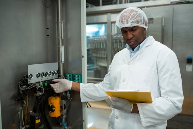 Trabajador sosteniendo el portapapeles mientras opera la máquina en la fábrica de jugos