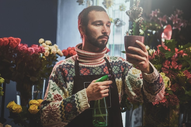 El trabajador de la tienda de flores se ocupa de los cactus, rodeado de hermosas flores.