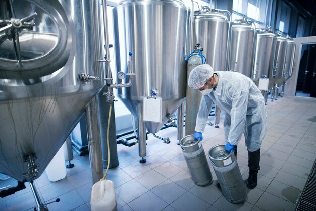 Trabajador en traje de protección que transporta productos químicos en depósitos metálicos