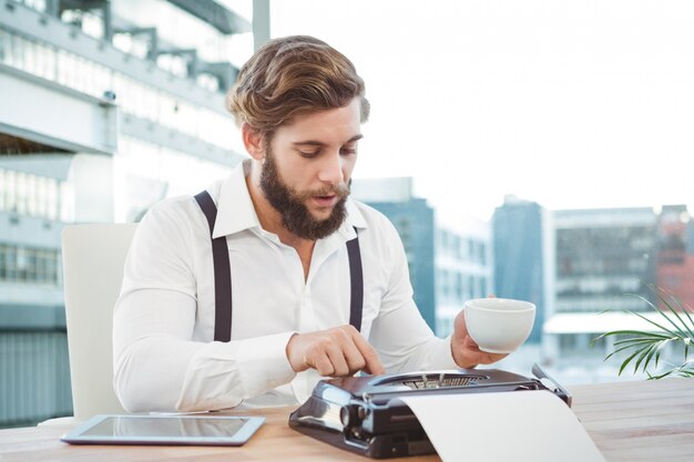 Trabajador usando una máquina de escribir mientras toma un café