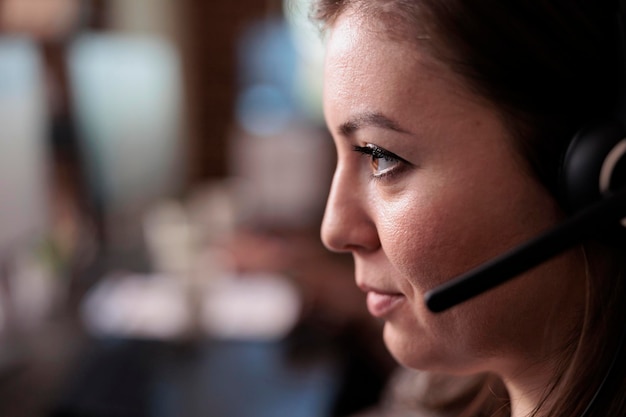 Trabajador de ventas de telemarketing que responde a la llamada del cliente en el auricular, hablando con personas en soporte de línea de ayuda remota. Operador de teletrabajo joven que utiliza equipos de servicio de atención al cliente. De cerca.