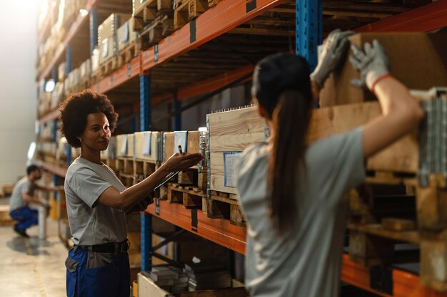 Trabajadora afroamericana comunicándose con su colega mientras prepara el envío en un almacén industrial