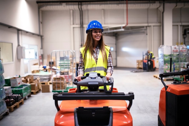 Foto gratuita trabajadora de almacén con casco y equipo de seguridad reflectante que conduce una máquina elevadora en un gran centro de almacén de distribución