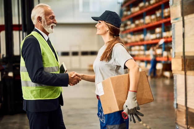 Trabajadora de almacén feliz apretón de manos con el gerente de la empresa en el compartimento de almacenamiento industrial