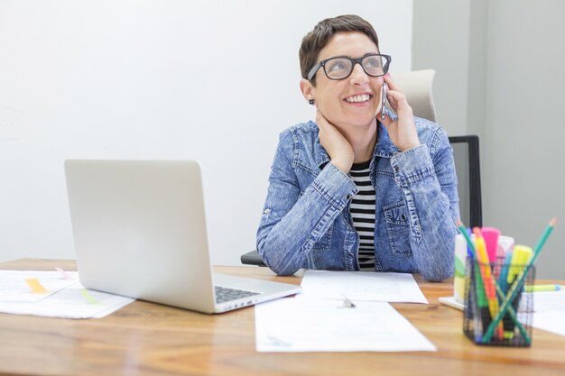 Trabajadora feliz mirando hacia arriba y hablando por teléfono