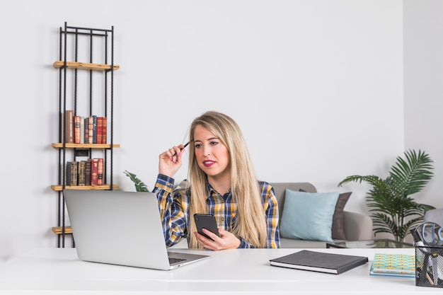 Foto gratuita trabajadora mirando portátil y sosteniendo teléfono móvil