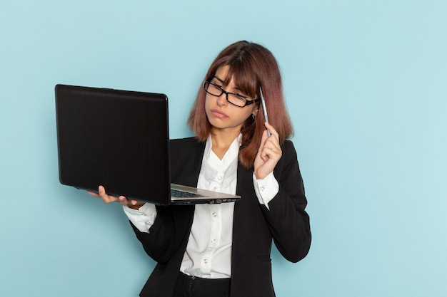 Trabajadora de oficina vista frontal en traje estricto usando una computadora portátil y pensando en una superficie azul claro