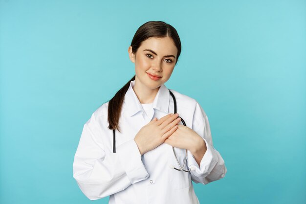 Trabajadora de la salud cariñosa joven doctora cogidos de la mano en el corazón y sonriendo mirando con cuidado y...