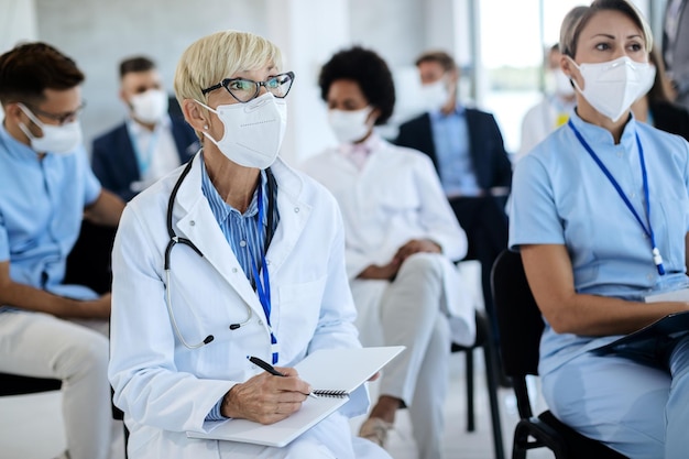 Trabajadora de la salud madura tomando notas en su cuaderno durante un seminario en la sala de juntas