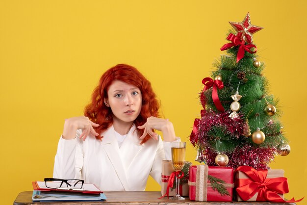 Trabajadora sentada detrás de su mesa con árbol de Navidad y regalos en amarillo