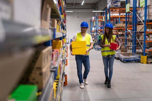 Trabajadores del almacén con cascos y chaquetas reflectantes llevando cajas en un gran centro de distribución