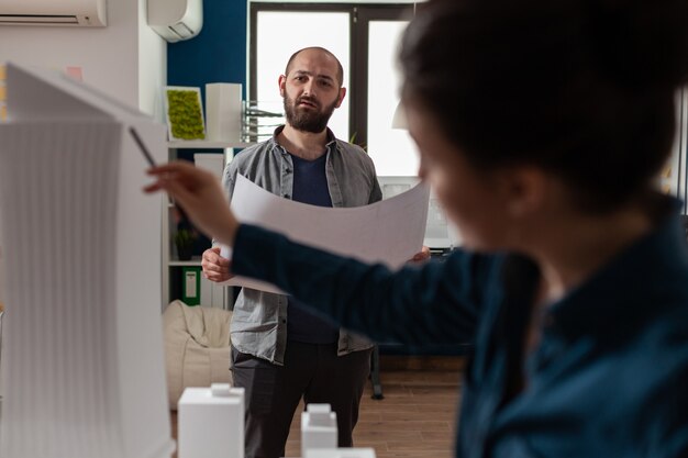 Trabajadores de arquitectura comprobando planos con maqueta