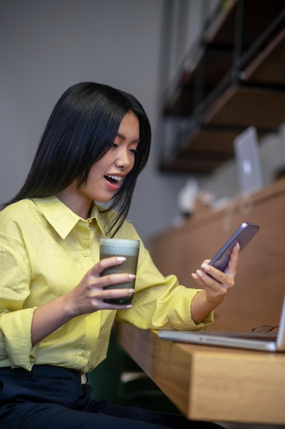 Trabajadores por cuenta propia. Bastante joven mujer asiática en camisa amarilla trabajando en una computadora portátil