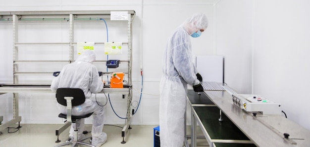 Trabajadores de fábrica con trajes de laboratorio blancos y máscaras faciales que producen televisores con algunos equipos modernos