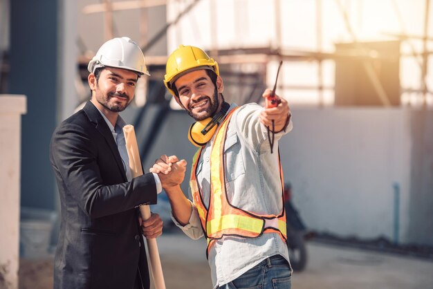 Trabajadores felices en el sitio de construcción joven ingeniero civil gerente y arquitectos que se dan la mano en el sitio de construcción y buscan el concepto de trabajo en equipo de cooperación de la próxima fase de construcción