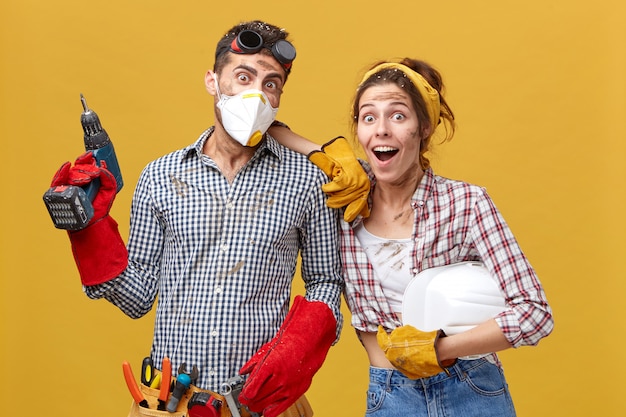 Los trabajadores de mantenimiento vistiendo ropa casual sosteniendo equipos de construcción con una mirada de sorpresa sin creer sus ojos que terminaron su trabajo tan rápido. Concepto de trabajo en equipo y rapidez