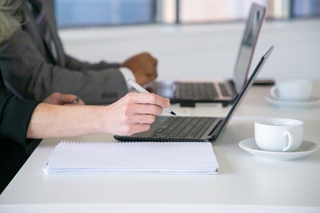 Trabajadores de oficina escribiendo notas, usando la computadora portátil en la mesa con tazas de café. Primer plano de manos, tiro recortado. Concepto de educación o comunicación digital