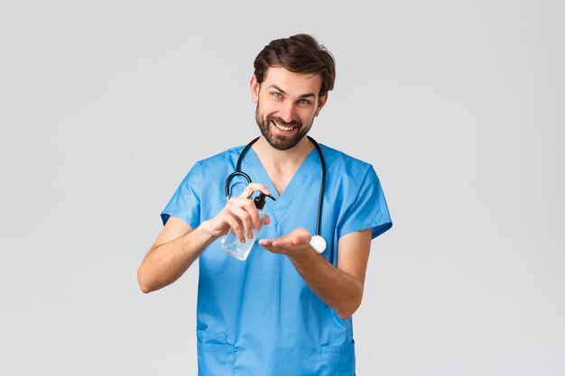 Trabajadores de la salud, concepto de brote de pandemia y coronavirus. Hombre sonriente que muestra cómo usar desinfectante de manos, jabón sqeeze en la palma y mira la cámara, fondo gris. Copia espacio