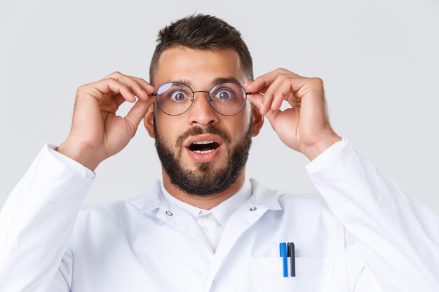 Trabajadores de la salud, coronavirus, pandemia de covid-19 y concepto de seguro. Primer plano de médico hispano emocionado e impresionado en bata blanca, ponerse gafas jadeando y mirando asombrado.