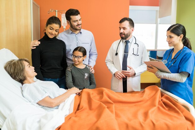 Trabajadores de la salud masculinos y femeninos que explican la enfermedad a un paciente mayor con su familia en el hospital