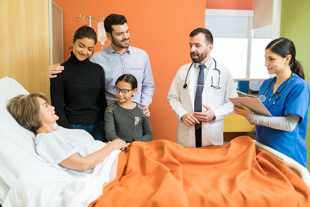 Trabajadores de la salud masculinos y femeninos que explican la enfermedad a un paciente mayor con su familia en el hospital