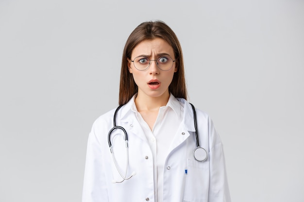Trabajadores de la salud, medicina, seguros y concepto de pandemia covid-19. Doctora nerviosa sorprendida en batas blancas y gafas, médico jadeando y mirando fijamente a la cámara preocupada