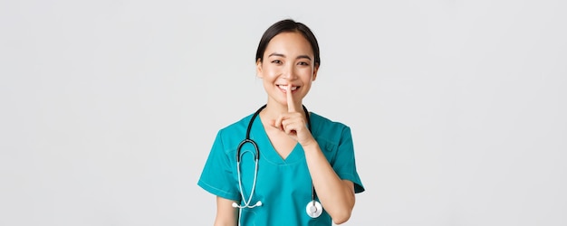 Trabajadores de la salud, prevención de virus, concepto de campaña de cuarentena. Doctor asiático sonriente, enfermera con uniformes médicos sonriendo, callando, pidiendo silencio, de pie con fondo blanco