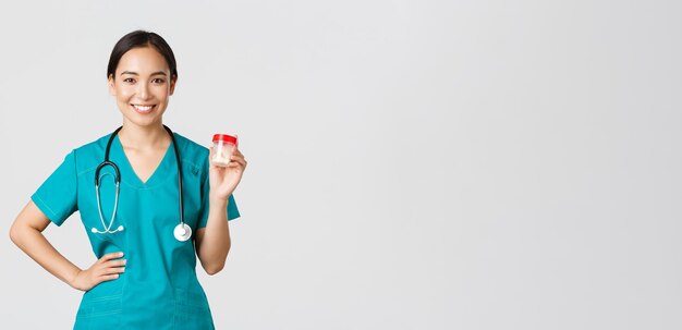 Trabajadores de la salud, prevención de virus, concepto de campaña de cuarentena. Sonriente doctora bastante asiática, enfermera en matorrales mostrando pastillas, recomendar medicamentos o vitaminas, fondo blanco.