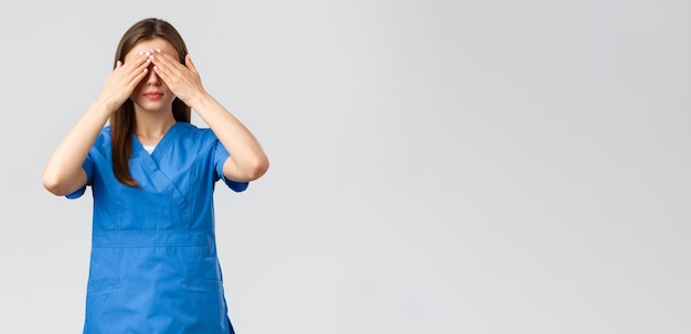 Foto gratuita los trabajadores de la salud previenen el seguro contra virus y el concepto de medicina mujer joven con bata azul médico o enfermera cierra los ojos con las manos con los ojos vendados medicina de pie fondo gris