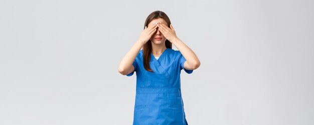 Los trabajadores de la salud previenen el seguro de virus y el concepto de medicina Mujer joven con bata azul médico o enfermera cierra los ojos con las manos con los ojos vendados medicina de pie fondo gris