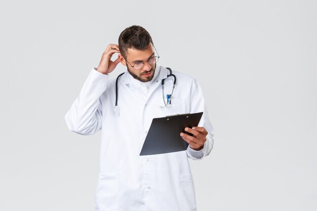 Trabajadores de la salud, seguro médico, laboratorio clínico y concepto de covid-19. Médico joven pensativo en matorrales, gafas, estudiando el archivo del paciente, rascarse la cabeza y mirar el portapapeles, leer documentos.