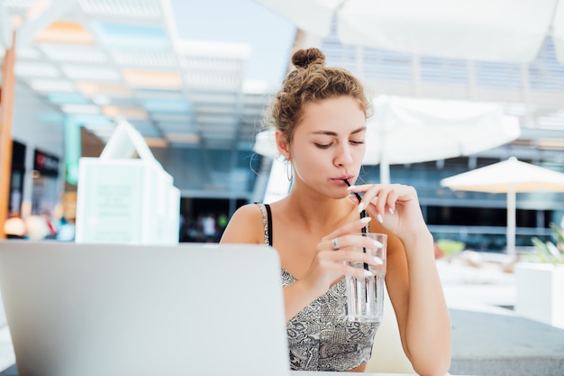 Trabajando al aire libre. Hermosa mujer joven con funky hat trabajando en una computadora portátil y sonriendo mientras está sentado al aire libre