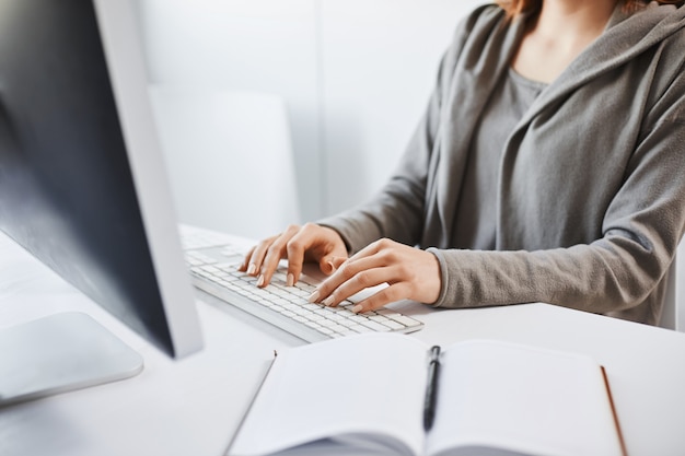 Trabajando duro para festejar los fines de semana. Captura recortada de mujer escribiendo en el teclado, sentado frente al monitor de la computadora. Freelancer traduce un nuevo proyecto y escribe algunas notas en el bloc de notas.