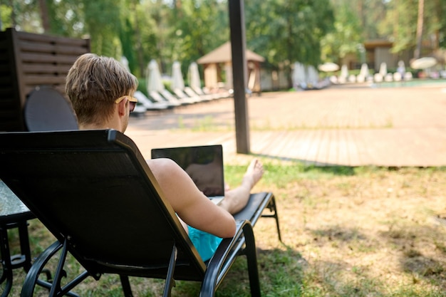 Trabajar y descansar. Un hombre sentado en una tumbona y trabajando en una computadora portátil