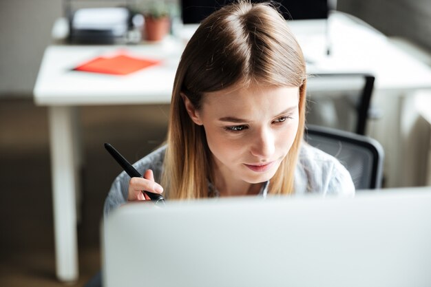 Trabajo concentrado de la mujer joven en la oficina usando la computadora