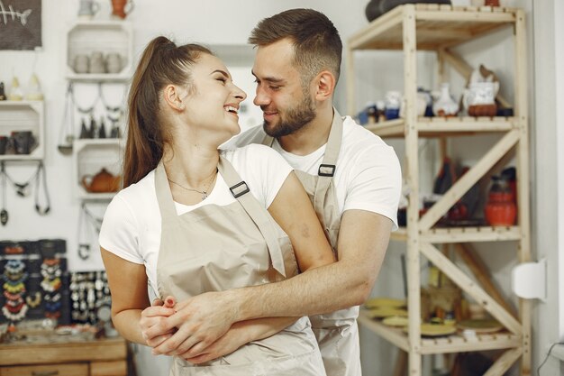 Trabajo creativo mutuo. Hermosa joven pareja en ropa casual y delantales. La gente tiene platos de cerámica.