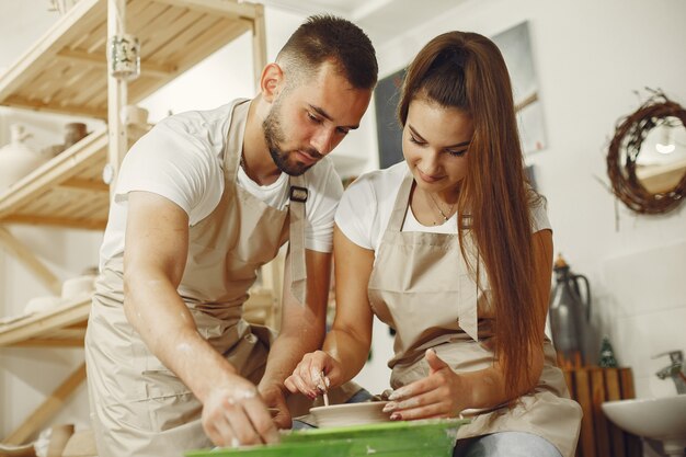 Trabajo creativo mutuo. Hermosa joven pareja en ropa casual y delantales. Personas creando un cuenco en un torno de alfarería en un taller de arcilla.