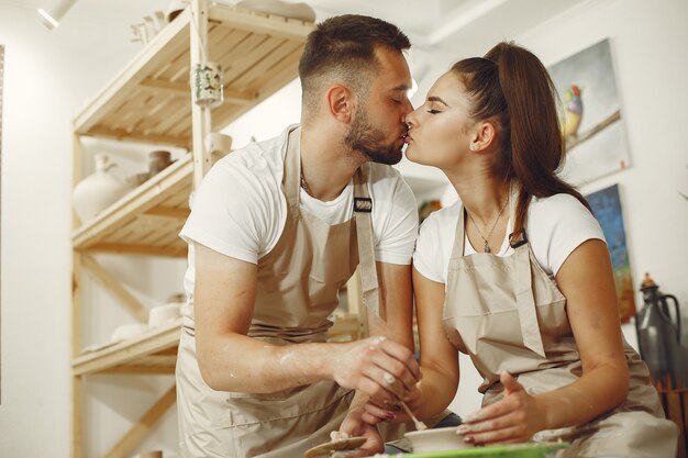 Trabajo creativo mutuo. Hermosa joven pareja en ropa casual y delantales. Personas creando un cuenco en un torno de alfarería en un taller de arcilla.