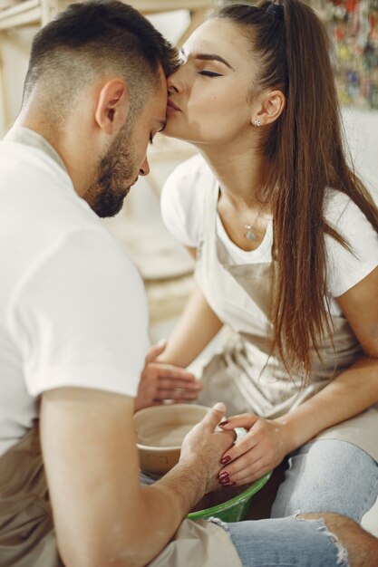 Trabajo creativo mutuo. Hermosa joven pareja en ropa casual y delantales. Personas creando un cuenco en un torno de alfarería en un taller de arcilla.