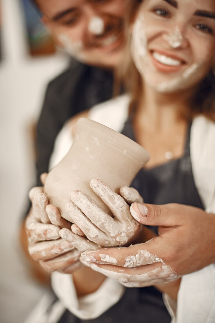 Foto gratuito trabajo creativo mutuo. hermosa joven pareja en ropa casual y delantales. personas creando un cuenco en un torno de alfarería en un taller de arcilla.