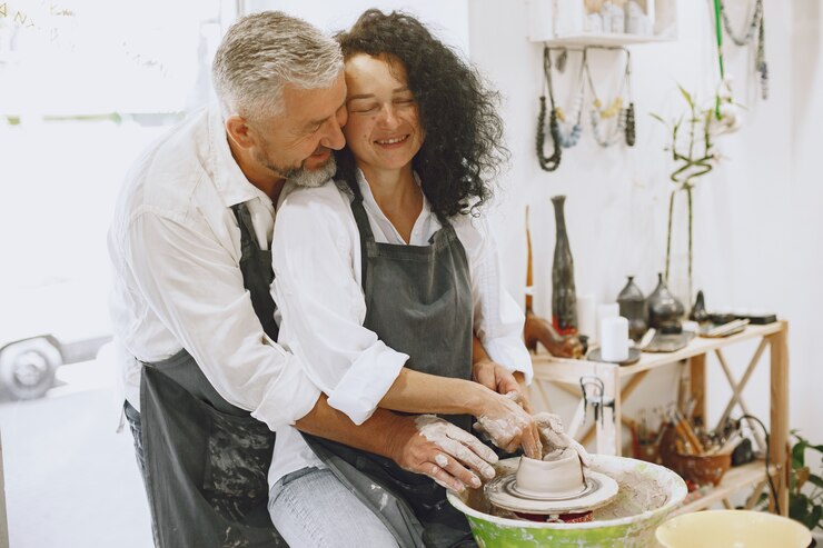 Foto gratuito trabajo creativo mutuo. pareja adulta elegante en ropa casual y delantales. personas creando un cuenco en un torno de alfarería en un taller de arcilla.