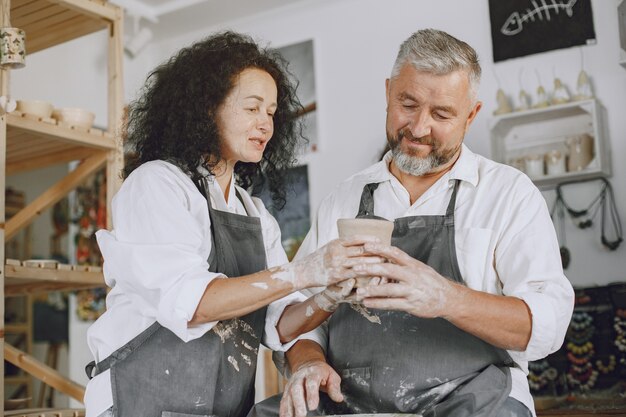 Trabajo creativo mutuo. Pareja adulta elegante en ropa casual y delantales. Personas creando un cuenco en un torno de alfarería en un taller de arcilla.