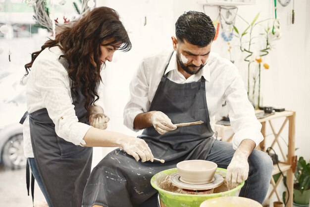 Trabajo creativo mutuo. Pareja elegante en ropa casual y delantales. Personas creando un cuenco en un torno de alfarería en un taller de arcilla.