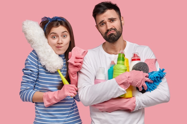 Foto gratuita trabajo en equipo y concepto de limpieza. el hombre y la mujer joven disgustados ven la habitación sucia con disgusto, usan productos de limpieza