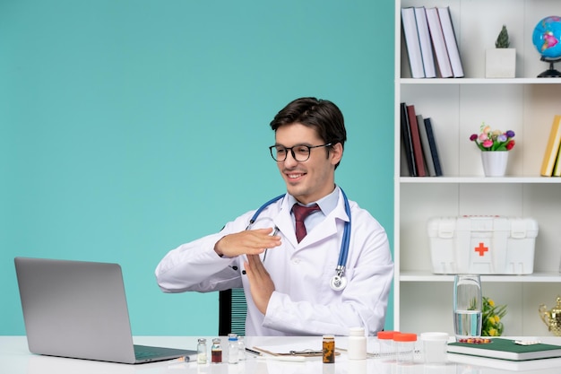 Trabajo médico en la computadora remotamente serio lindo lindo médico inteligente en bata de laboratorio que muestra el signo de finalización