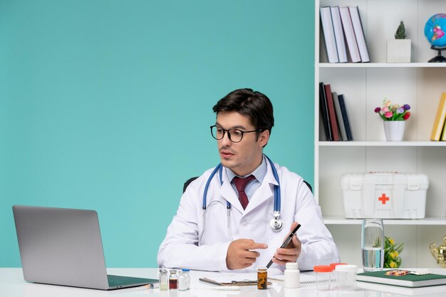 Trabajo médico de forma remota en la computadora serio lindo médico inteligente en bata de laboratorio escribiendo notas